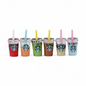 Pu&ograve; includere: Sei mini bevande al t&egrave; alle bolle in stile Starbucks in fila, ognuna con un liquido di colore diverso e una cannuccia. Le bevande sono in bicchieri di plastica trasparente con il logo Starbucks. I colori includono rosso, arancione, verde, marrone, giallo e blu.
