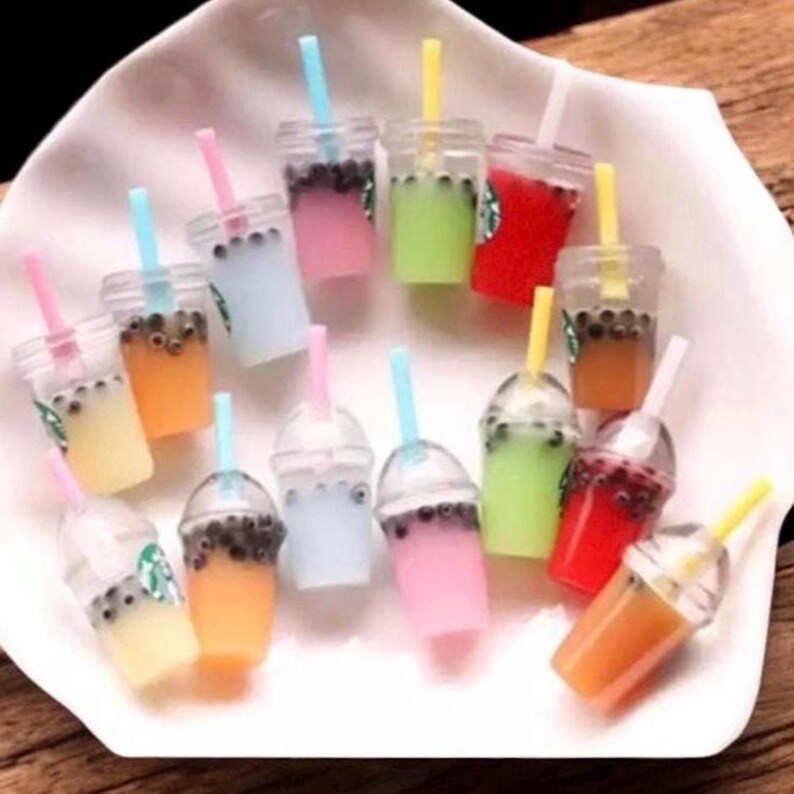Pu&ograve; includere: Miniature bevande al bubble tea colorate con cannucce. Le bevande sono in bicchieri di plastica trasparente con vari colori pastello, tra cui rosa, blu, verde e arancione. Alcune tazze hanno un logo Starbucks.