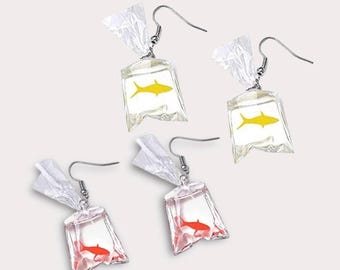 May include: Four dangle earrings featuring clear, crinkled plastic bag charms. Two earrings contain a yellow fish graphic, and two earrings contain a red fish graphic. Each charm is suspended from a silver-toned metal hook for pierced ears.