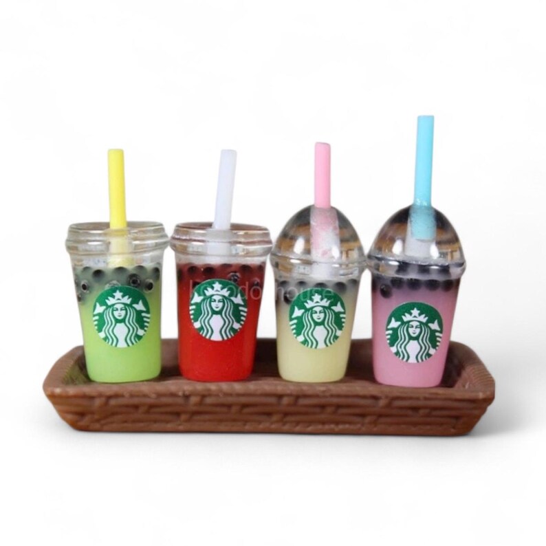 Pu&ograve; includere: Quattro miniature di bubble tea in bicchieri trasparenti con cannucce, presentate su un vassoio marrone. Le bevande sono verdi, rosse, gialle e rosa, ognuna con un logo Starbucks. Le cannucce sono gialle, bianche, rosa e blu.
