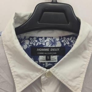 Puede incluir: Una taza de cer&aacute;mica blanca con un asa negra y el texto "But First, Coffee" en negro, con una fuente de estilo manuscrito. La taza est&aacute; sobre una superficie blanca.