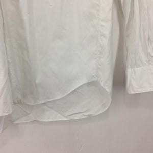 Puede incluir: Primer plano de una camisa blanca abotonada. La camisa est&aacute; hecha de una tela ligera y presenta mangas largas con pu&ntilde;os abotonados. El dobladillo inferior es curvo.