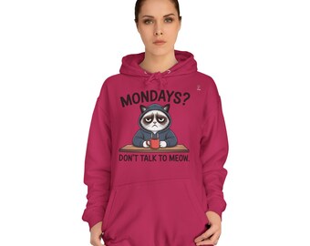 Puede incluir: Una sudadera con capucha magenta con cordón y un gráfico de un gato gruñón con el texto "MONDAYS? DON'T TALK TO MEOW." El gato está representado con una sudadera con capucha y una taza de café.