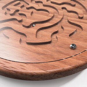 May include: A wooden circular maze game with a metal ball inside. The maze is carved into the wood and has a clear plastic cover.