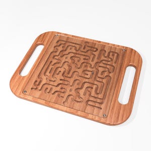 May include: A wooden maze game with a clear acrylic top and two handles. The maze is made of a light brown wood and has a complex design.