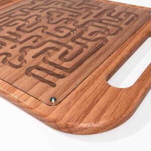 May include: A wooden tray with a glass insert featuring a maze design. The tray has a rounded edge and a handle on the side.