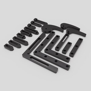 May include: A set of black plastic corner brackets and other hardware pieces for woodworking projects. The pieces are arranged on a white surface.