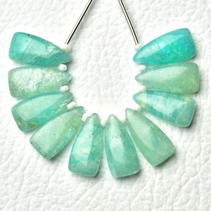 May include: A collection of turquoise gemstone beads. Each bead has a unique shape and a faceted surface that reflects light. The beads are strung on a thin silver wire, creating a delicate appearance. The beads are arranged in a semi-circle, with a light background.