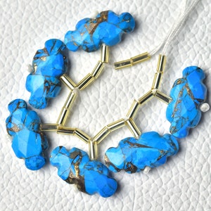May include: A strand of turquoise gemstone beads with gold accents. The beads are irregularly shaped and have a cloudy, blue colour. The beads are strung on a white cord with gold spacers.