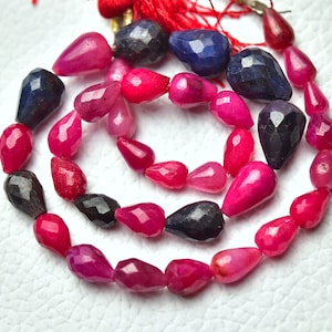 Op de afbeelding: Een streng facetgeslepen edelsteen kralen in tinten roze en blauw. De kralen zijn druppelvormig en geregen aan een koord.