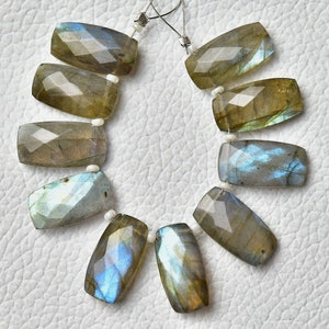May include: A strand of ten faceted labradorite gemstone beads in a rectangular shape. The beads are a mix of grey, brown, and blue colours with iridescent flashes.