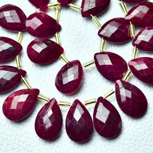 Op de afbeelding: Een streng dieprode robijn edelsteen kralen in een druppelvorm. De kralen zijn gefacetteerd en geregen op goudkleurig draad.