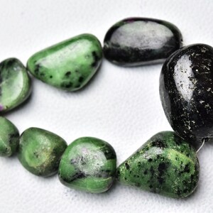 Könnte beinhalten: Eine Kette aus grünen und schwarzen Edelsteinperlen. Die Perlen sind glatt und poliert und haben ein natürliches, organisches Aussehen. Die Perlen sind auf einem dünnen Draht aufgefädelt.