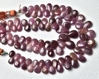 May include: A strand of pink ruby gemstone beads in a teardrop shape. The beads are strung on a cord with a tassel at one end.