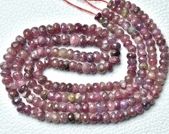 May include: A strand of pink and purple faceted gemstone beads. The beads are small and round, and they are strung on a thin thread. The beads are arranged in a loose, flowing pattern.