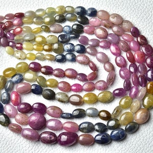 May include: A strand of oval-shaped gemstone beads in shades of blue, pink, and yellow. The beads are arranged in a circular pattern, with the different colors creating a rainbow effect.