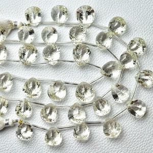May include: A strand of clear quartz gemstone beads with a faceted, teardrop shape. The beads are strung on a silver wire and have a natural, translucent appearance.