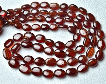 May include: A strand of oval-shaped, reddish-brown gemstone beads. The beads are smooth and polished, with a slight sheen.