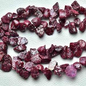 May include: A strand of deep red ruby gemstone beads, each bead is irregularly shaped and has a slightly iridescent finish.