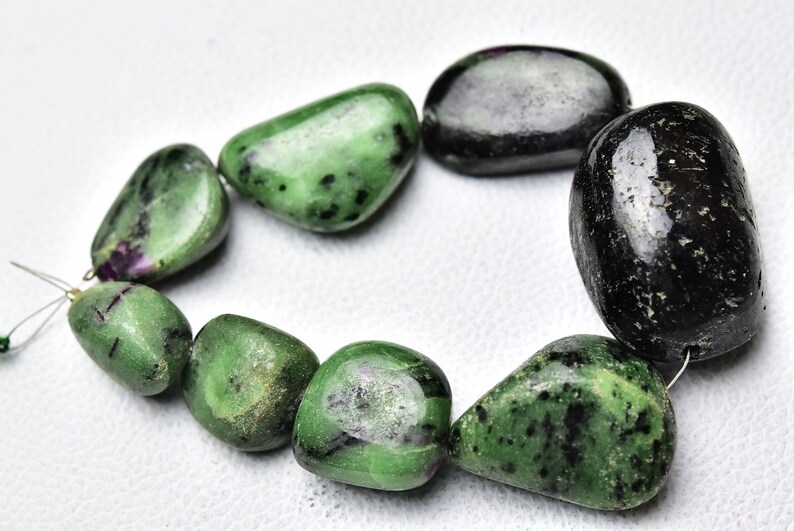 May include: A strand of green and black gemstone beads. The beads are smooth and polished, and they have a natural, organic look. The beads are strung on a wire, and they are ready to be used in jewelry making.