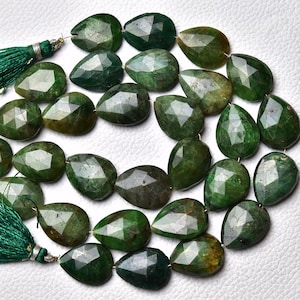 May include: A strand of green gemstone beads, each bead is faceted and shaped like a teardrop. The beads are strung on a silver wire and have a green tassel on each end.