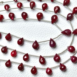 May include: A strand of ruby red gemstone beads in a teardrop shape. The beads are strung on silver wire.