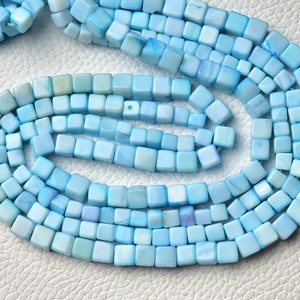 Puede incluir: Una hebra de cuentas cuadradas de color azul claro hechas de concha. Las cuentas miden aproximadamente 6 mm.