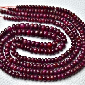 Puede incluir: Una hebra de cuentas de rubí rojo oscuro, cada cuenta es redonda y ligeramente irregular en forma. Las cuentas están enhebradas en un hilo delgado y están dispuestas en un patrón circular.