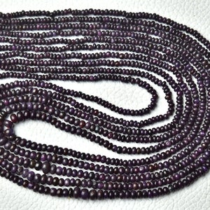 May include: A strand of purple gemstone beads, approximately 2mm in diameter, arranged in a circular pattern on a white surface.