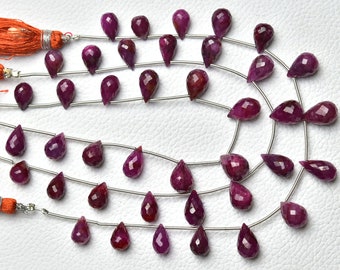 May include: A strand of ruby gemstone beads in a teardrop shape. The beads are strung on a silver wire and are a deep red color.