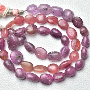 May include: A strand of pink and purple gemstone beads. The beads are oval shaped and have a smooth, polished finish.