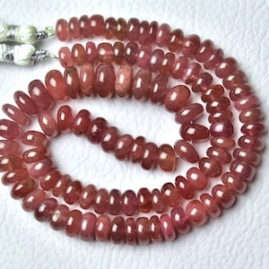 Peut inclure: Collier de perles de pierres précieuses polies, de couleur brun rougeâtre. Les perles ovales sont enfilées, avec un pompon à l'extrémité. Les perles ont une finition brillante et varient légèrement en couleur.