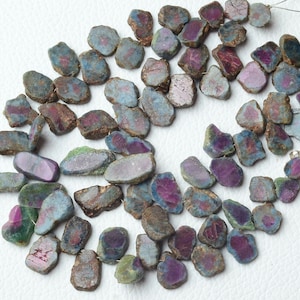 May include: A strand of loose, irregular shaped, green, blue, and pink gemstone beads. The beads are all different sizes and shapes, and they have a rough, natural look.