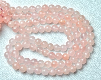 Può includere: Una collana di perle di quarzo rosa pallido. Le perle sono rotonde e lisce e sono infilate su un filo elastico trasparente.