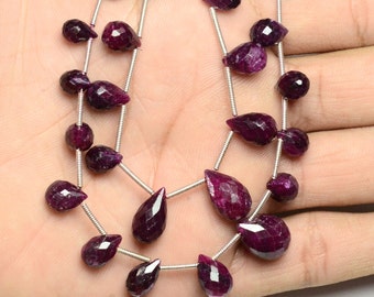 May include: A strand of deep purple gemstone beads, each bead is faceted and shaped like a teardrop. The beads are strung on a silver wire.