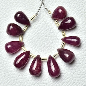 May include: A strand of 12 teardrop-shaped ruby beads, each with a smooth, polished surface. The beads are strung on a wire with gold-coloured spacers.