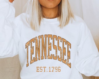 Op de afbeelding: Witte trui met een bruine vintage-stijl grafische afbeelding met de tekst "Tennessee Est. 1796".