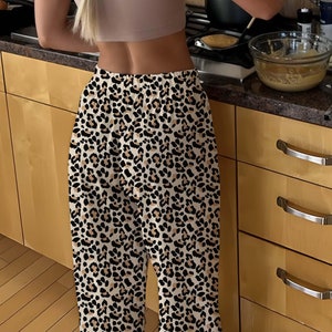 Op de afbeelding: Een persoon draagt een beige tanktop en een broek met luipaardprint en kookt in een keuken. De persoon roert een kom beslag met een houten lepel.