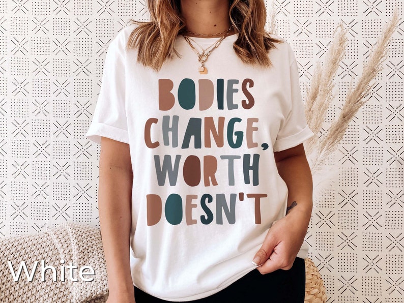 May include: White t-shirt with the text "BODIES CHANGE, WORTH DOESN'T" in colorful block letters.