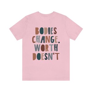 May include: Pink t-shirt with the text "BODIES CHANGE, WORTH DOESN'T" in colorful, stylized lettering.