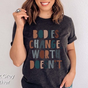 May include: Dark grey heather t-shirt with the text "BODIES CHANGE, WORTH DOESN'T" in colorful block letters.