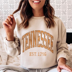 Puede incluir: Una sudadera beige con un gr&aacute;fico marr&oacute;n de estilo vintage que dice "Tennessee Est. 1796".