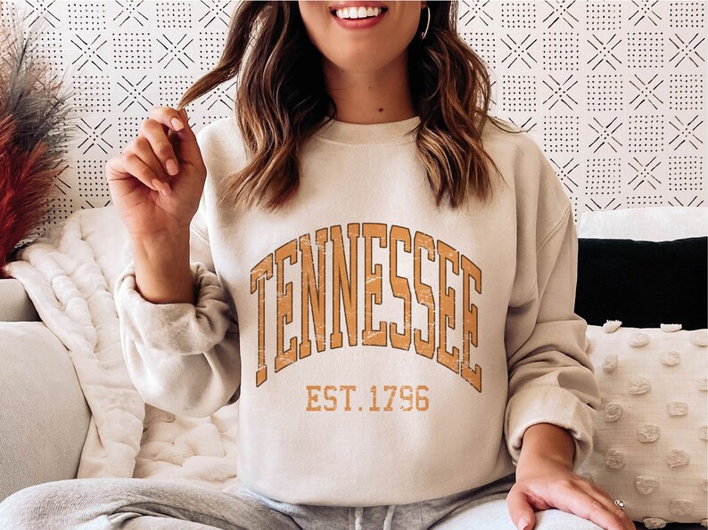 Puede incluir: Una sudadera beige con un gr&aacute;fico marr&oacute;n de estilo vintage que dice "Tennessee Est. 1796".