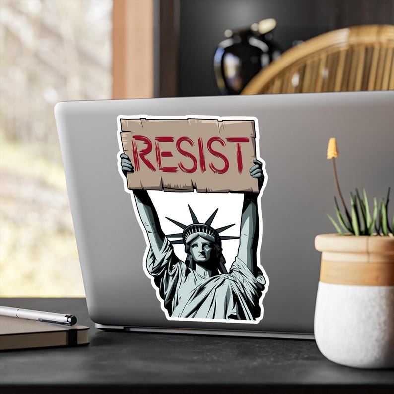 Puede incluir: Una pegatina con una ilustraci&oacute;n de dibujos animados de la Estatua de la Libertad sosteniendo un cartel que dice "RESIST".