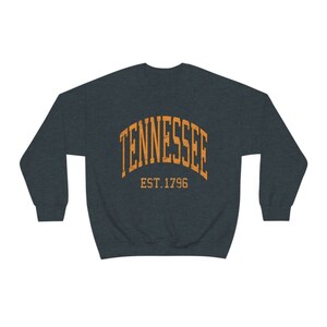 Puede incluir: Una sudadera azul oscuro con un dise&ntilde;o de arco naranja que dice "TENNESSEE EST. 1796".