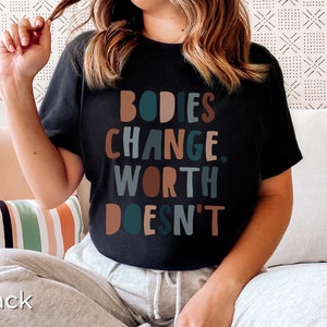 May include: A black t-shirt with the text "BODIES CHANGE, WORTH DOESN'T" in colorful letters.