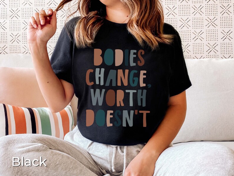 May include: A black t-shirt with the text "BODIES CHANGE, WORTH DOESN'T" in colorful letters.