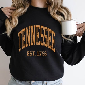 Puede incluir: Sudadera negra con un gr&aacute;fico naranja desgastado que dice "TENNESSEE EST. 1796".