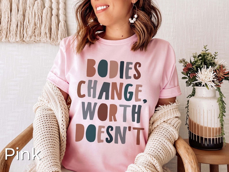 May include: Pink t-shirt with the text "BODIES CHANGE, WORTH DOESN'T" in colorful, stylized lettering.
