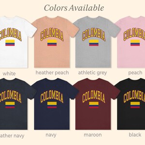 K&ouml;nnte beinhalten: Acht T-Shirts in verschiedenen Farben mit dem Wort "COLOMBIA" in Gelb und einer Grafik der kolumbianischen Flagge. Die Farben sind Wei&szlig;,  Heide-Pfirsich, Athletik-Grau, Pfirsich, Heide-Marine, Marine, Rotbraun und Schwarz.